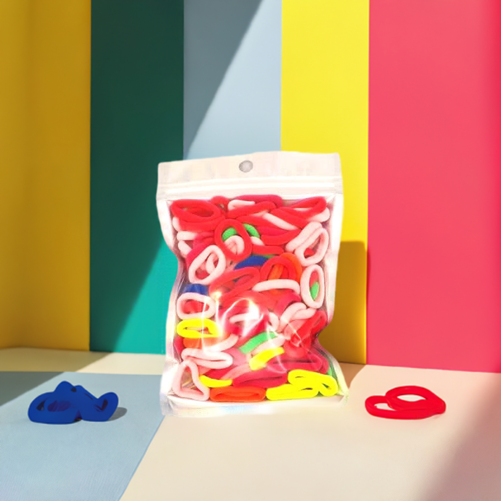 Baby & Toddler's Hair Ties: ENAX Hair Bands, One silver pack of (ENAX) colorful small sized Hair Ties. Mostly light and dark Pink coloured Hair Ties. 120 hair ties inside each pack, one pack in picture. Bold Stripe colourful background. Front Side.