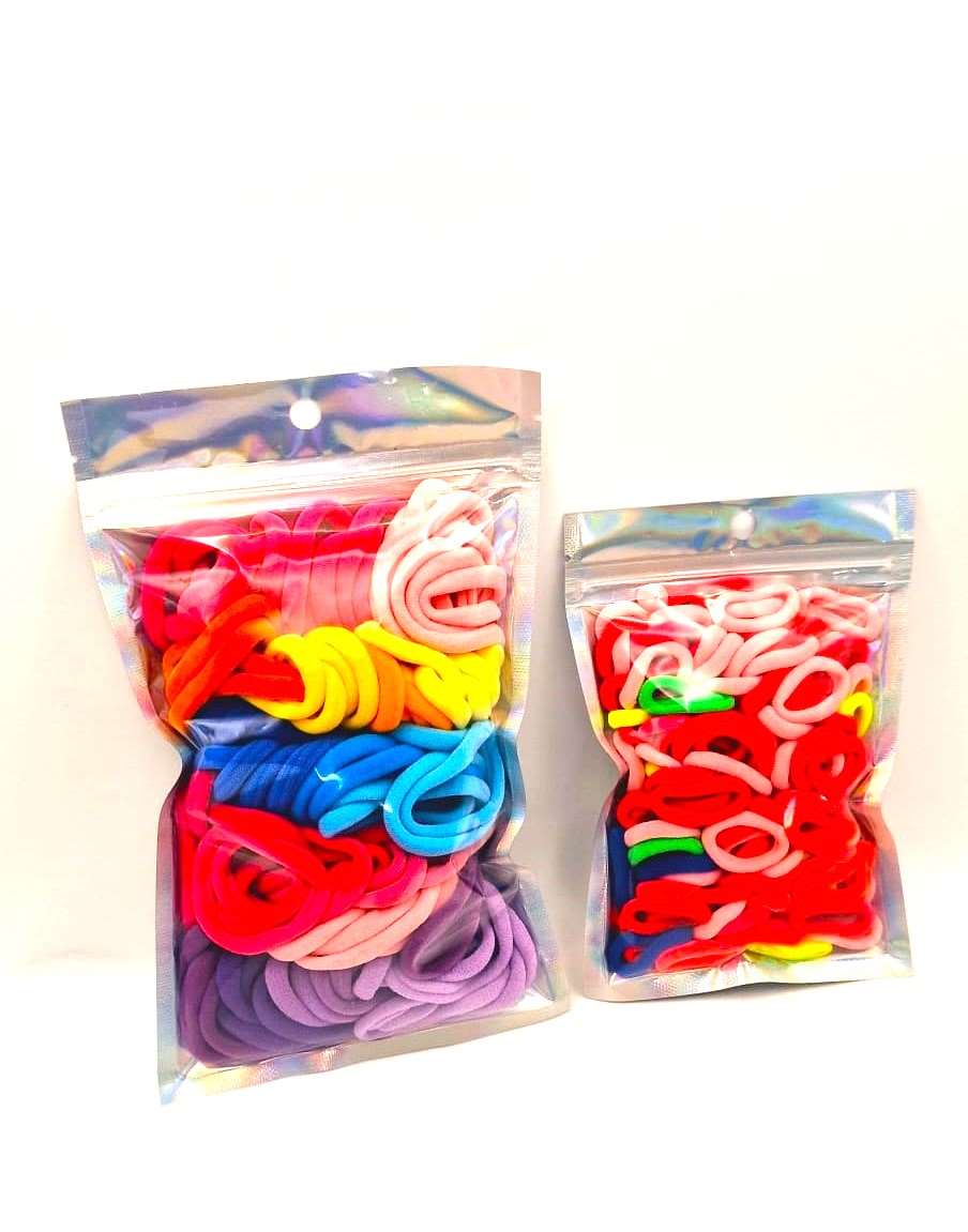 Girls & Baby's Hair Ties Pack of 2: ENAX Multi-Coloured Hair Bands. Two silver packets. First packet to the left consists of (ENAX) Girls Multi-Coloured, medium-sized Hair Ties. Second packet to the right consists of Baby & Toddler's Pink Hair Ties. 80 medium-sized Girls Multi-coloured hair ties and 120 Baby & Toddler's Pink Hair Ties, two packets inside picture. White background. Front Side.