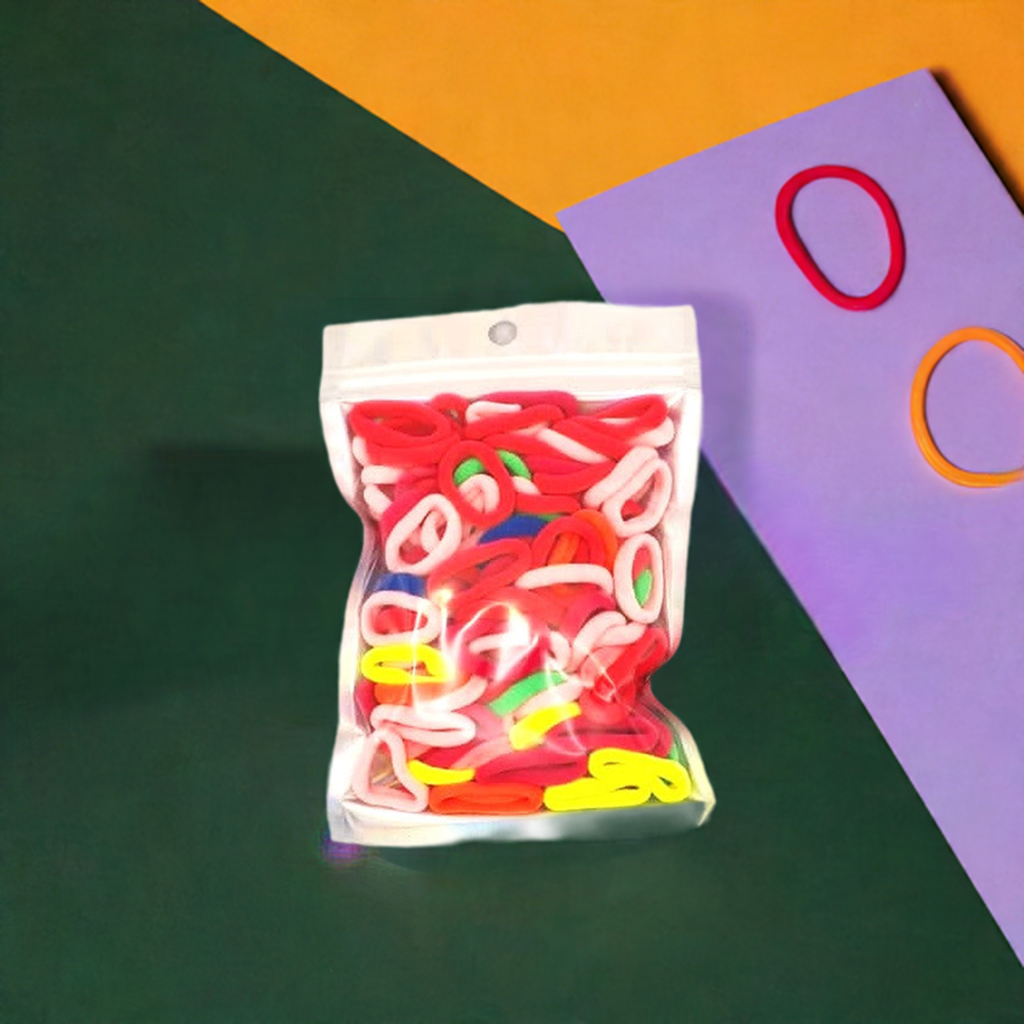 Baby & Toddler's Hair Ties: ENAX Hair Bands, One silver pack of (ENAX) colorful small sized Hair Ties. Mostly light and dark Pink coloured Hair Ties. 120 hair ties inside each pack, one pack in picture. Dark Green, Purple and Mustard background. Front Side.