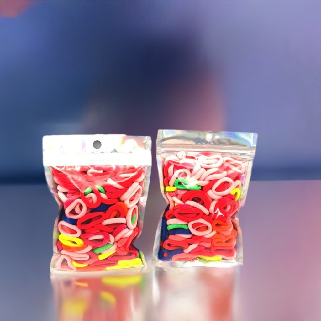 Baby & Toddler's Hair Ties Pack of 2: ENAX Hair Bands, Two silver packet of (ENAX) colorful small sized Hair Ties. Mostly light and dark Pink coloured Hair Ties. 120 hair ties inside each pack, two packets in picture. Blue and purple background. Transparent Front side.