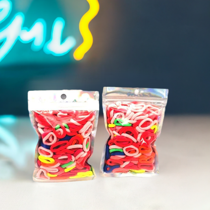 Baby & Toddler's Hair Ties Pack of 2: ENAX Hair Bands, Two silver packet of (ENAX) colorful small sized Hair Ties. Mostly light and dark Pink coloured Hair Ties. 120 hair ties inside each pack, two packets in picture. Dark Blue and Neon light background. Transparent Front side.