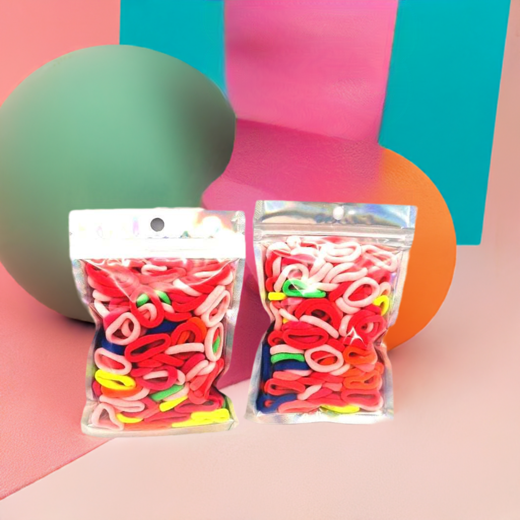 Baby & Toddler's Hair Ties Pack of 2: ENAX Hair Bands, Two silver packet of (ENAX) colorful small sized Hair Ties. Mostly light and dark Pink coloured Hair Ties. 120 hair ties inside each pack, two packets in picture. Bold, colourful geometric shapes background. Transparent Front side.